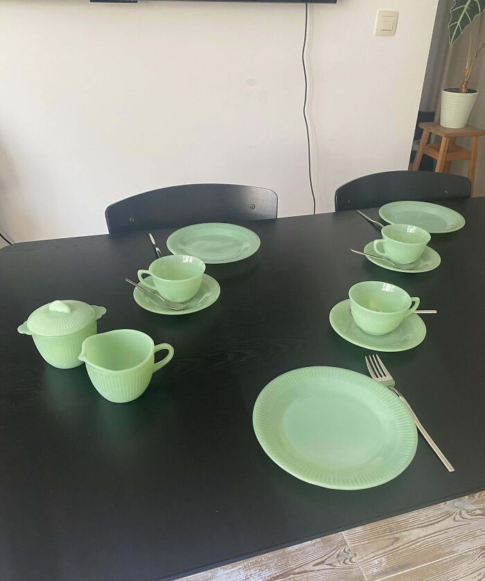 Vintage green glass tableware set with cups, saucers, and plates on a black table.