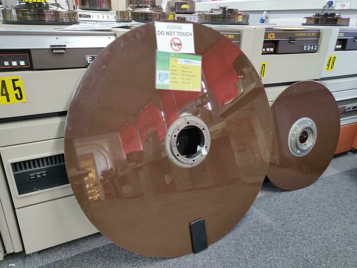 Large vintage computer hard disk on display, labeled with a sign "Please Do Not Touch," showcasing our world's fascinating history.
