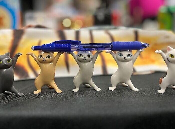 Mini cat figures holding a pen in an office setting, representing office Olympics creativity.