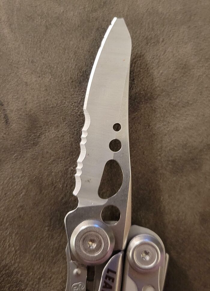 Multitool knife blade close-up on a textured surface, showcasing detailed edges and circular cutouts.