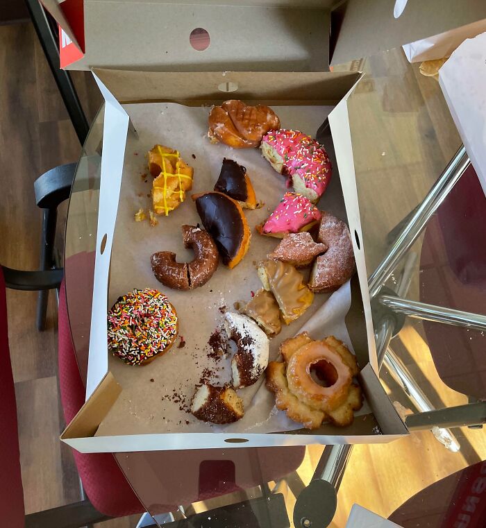 Box of leftover donuts, mostly eaten, on an office table, showcasing worst colleagues' indulgence.