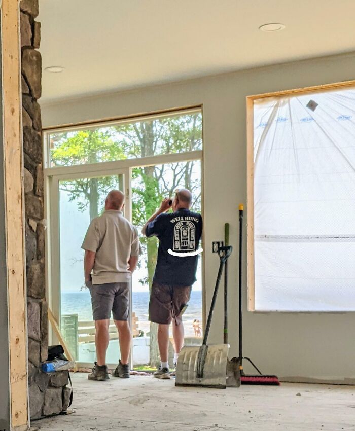 Two colleagues on a construction site, one in a "Well Hung" shirt, looking out a window.