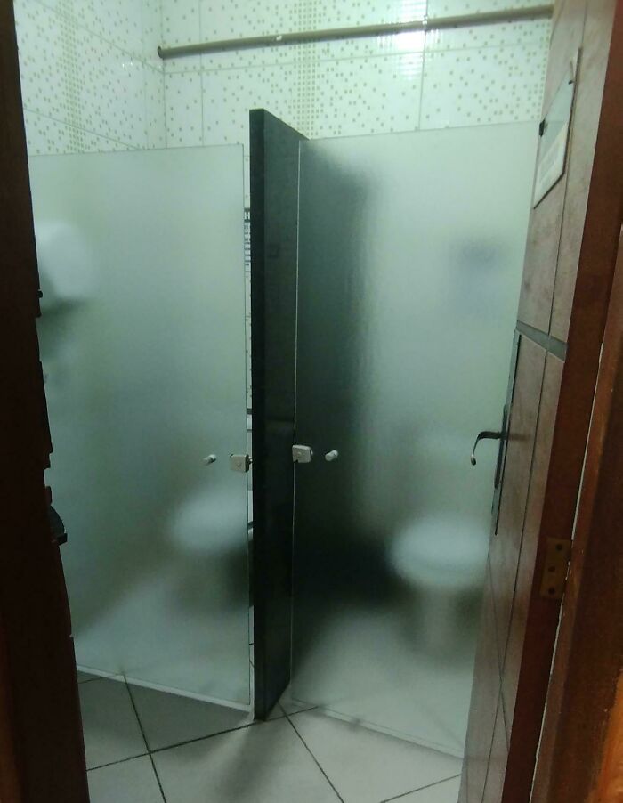 Frosted glass restroom stalls with peers visible, highlighting disastrous design.