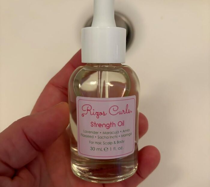 Hand holding a bottle of Rizos Curls Strength Oil.