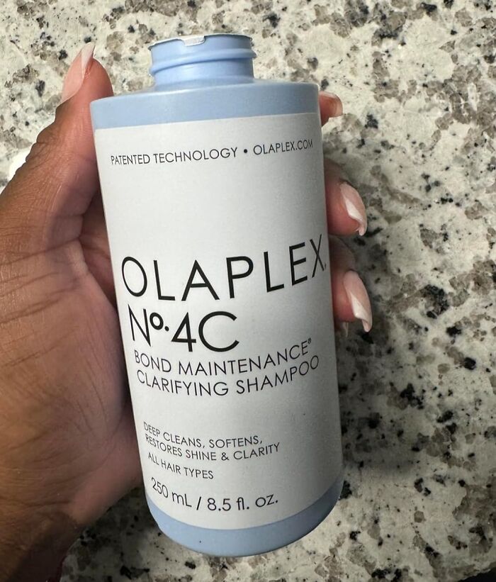 Olaplex No. 4C clarifying shampoo held by a hand on a marbled countertop, ideal for enhancing curls.