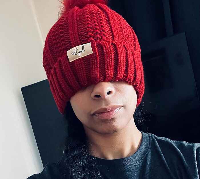 Person wearing a red knit hat with "curl" label covering eyes, highlighting life-changing curly hair fashion finds.