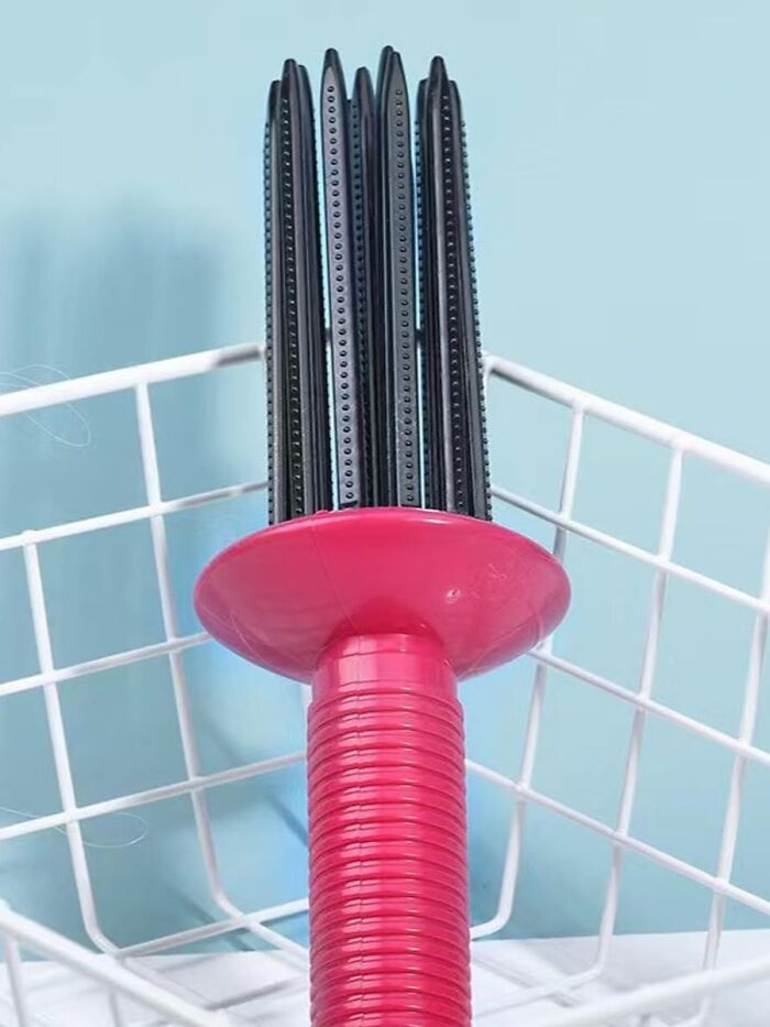 Pink curl tool with black bristles in a white wire basket against a blue background.