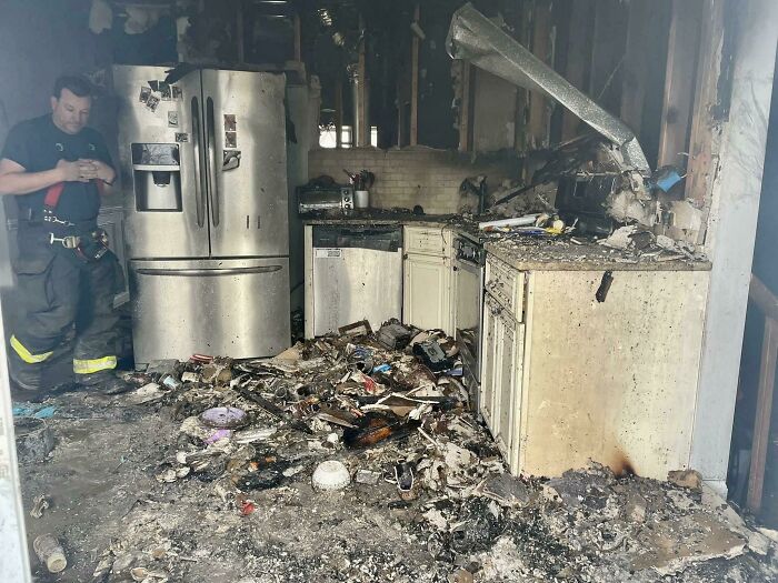 Firefighter surveys kitchen destroyed by fire, debris covering floor and appliances, illustrating poor decisions' impact on houses.