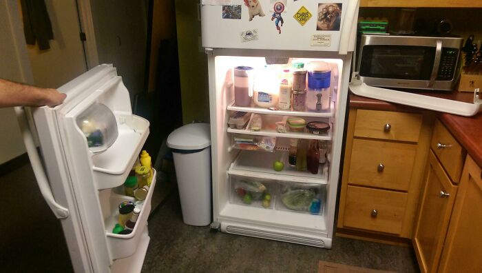 Open fridge in kitchen showing groceries and items, highlighting a poor design decision blocking the microwave.