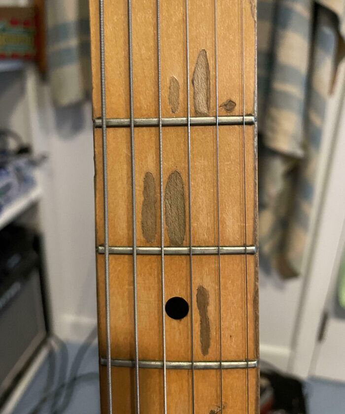 Close-up of a guitar neck with worn-down frets showing the effects of time on belongings.