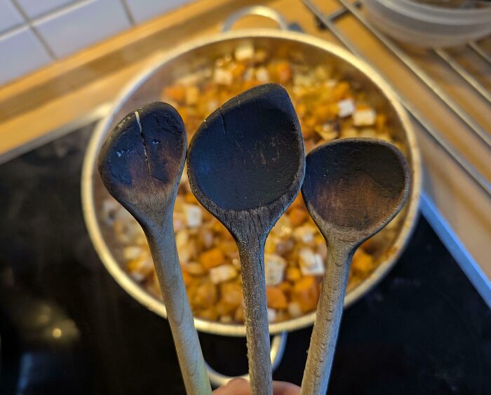 "Cucharas de madera desgastadas por el tiempo frente a una olla de guiso."