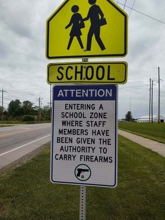 School zone sign stating staff can carry firearms, reflecting American schools' policies.