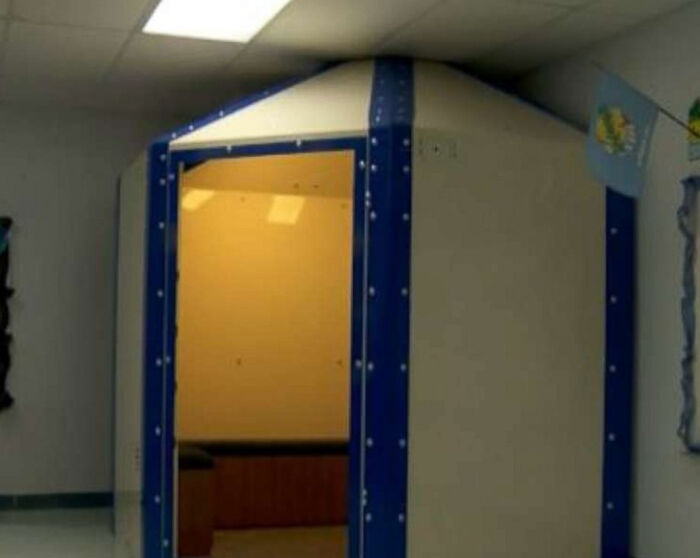 A blue-padded sensory room in an American school, with an open door showing a bench inside.
