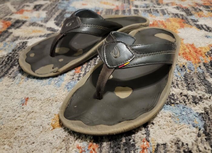 Worn-down black sandals on a colorful rug, showcasing the effects of time on people's belongings.