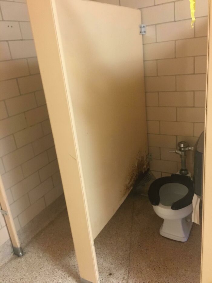 American school restroom with dirty stall, stained walls, and an unclean toilet seat.