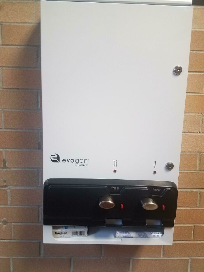 Sanitary product dispenser in an American school, offering free items against a brick wall.