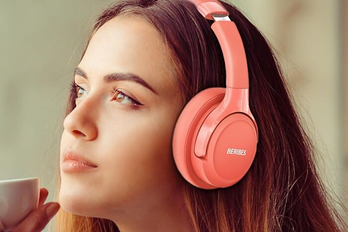 Woman wearing orange headphones, sipping coffee and gazing thoughtfully, embodying office olympics vibes.