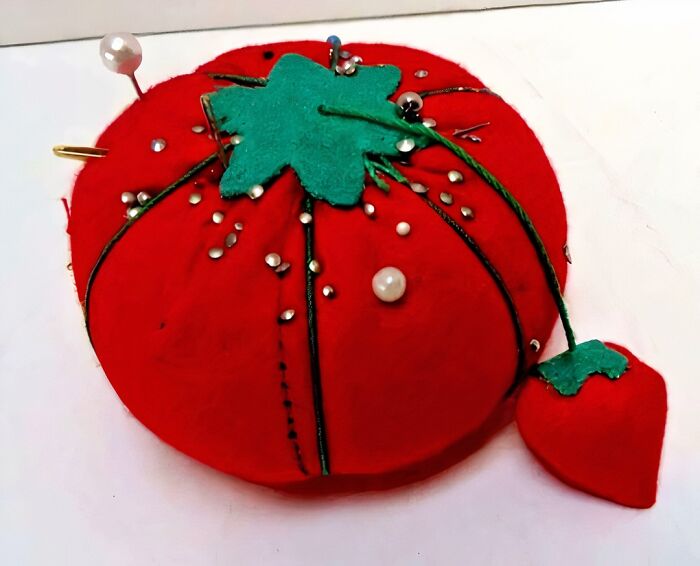 1980s vibe: red tomato-shaped pincushion with green leaf, decorated with pins.