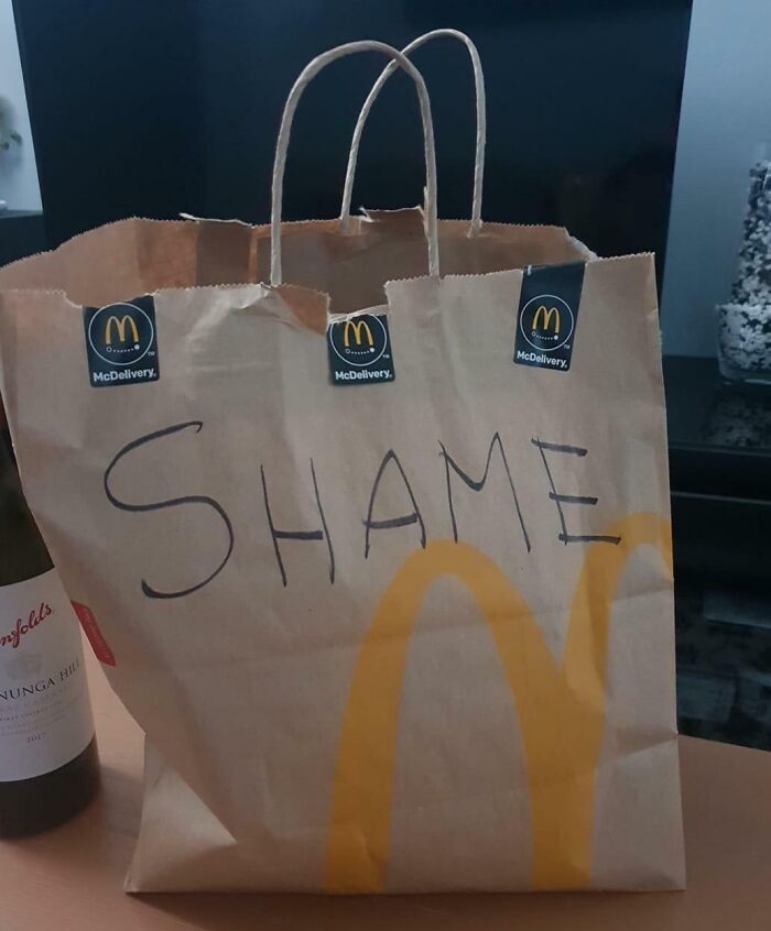McDelivery bag with "SHAME" written on it beside a wine bottle, symbolizing a bad day for someone.
