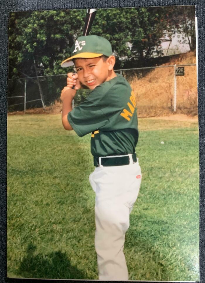 Niño en uniforme de béisbol posando con bate en un campo, mostrando un momento digno de compartirse en internet.