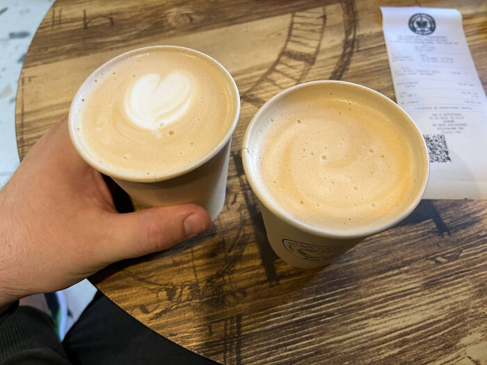 Two cups of latte on a wooden table, one with heart foam art, representing nothing interesting.