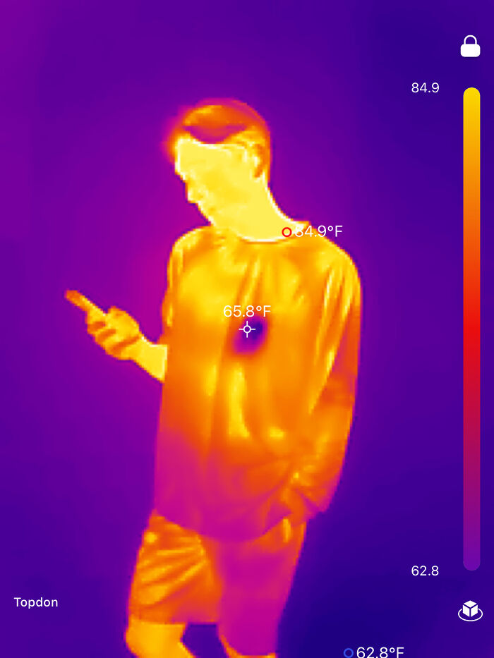 Thermal image of a person looking at their phone, displaying different temperature zones with bright colors.
