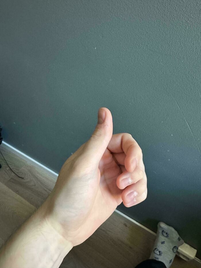 Close-up of a person's hand giving a thumbs-up in front of a plain wall, highlighting a mundane scene.
