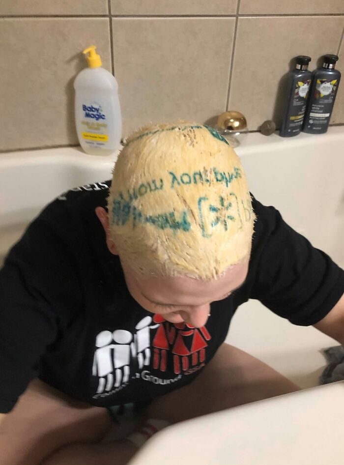 Persona con un error de tinte en el cabello en la bañera, mostrando letras verdes escritas accidentalmente.