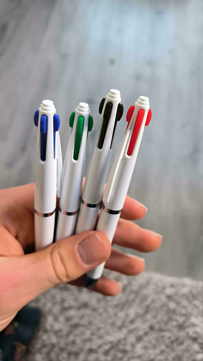 Four white multi-color pens held in a hand against a neutral background.