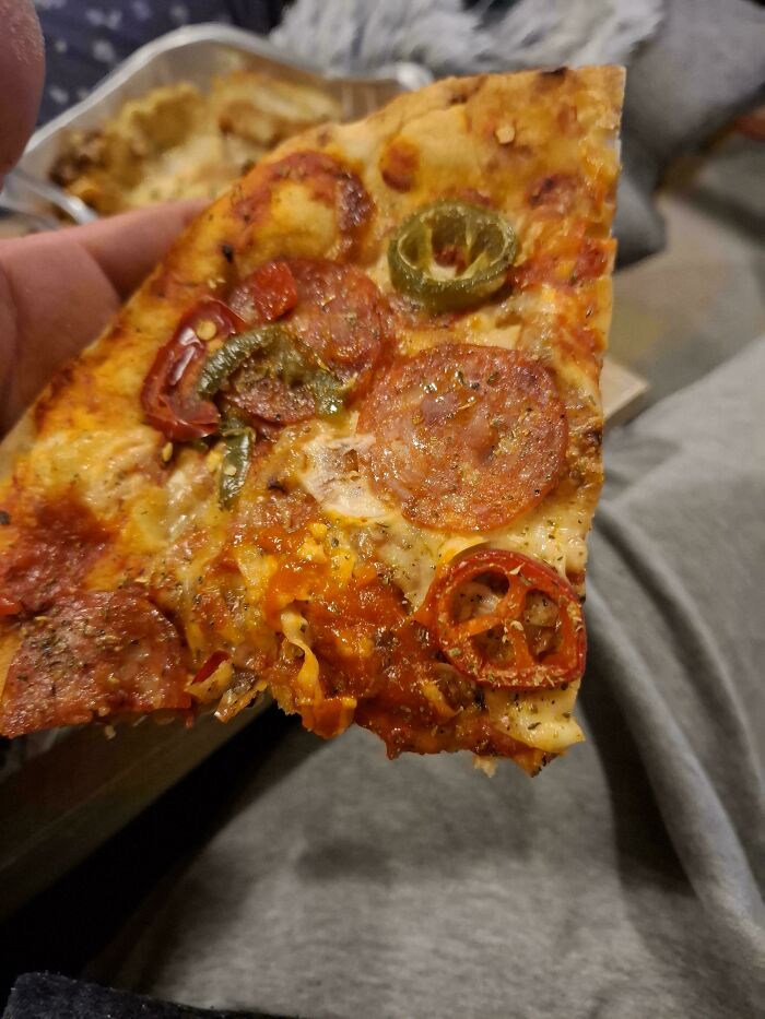 Close-up of a pepperoni pizza slice with jalapeños and tomatoes held in hand.