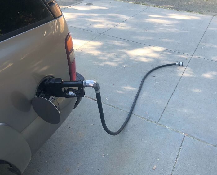 "Manguera de gasolina olvidada conectada a un coche estacionado, un error digno de compartirse en internet."