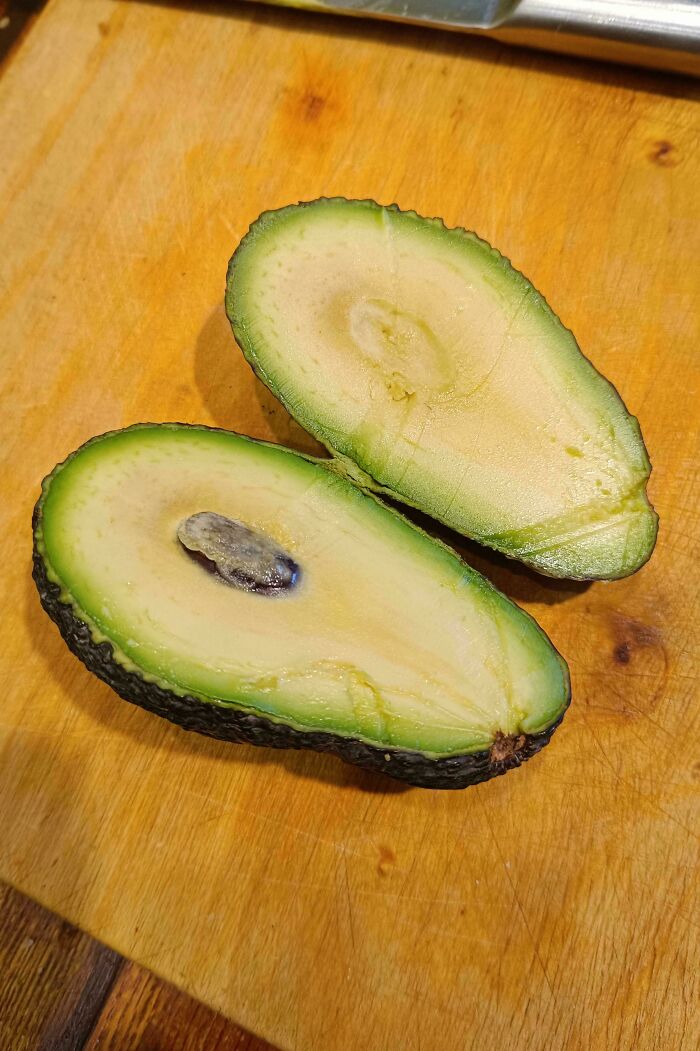 Sliced avocado on wooden board, showcasing its unremarkable texture and seed.