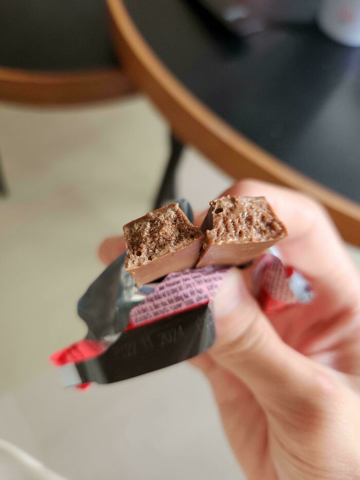 Close-up of a chocolate bar broken in half, held in a hand, showcasing an unremarkable snack moment.
