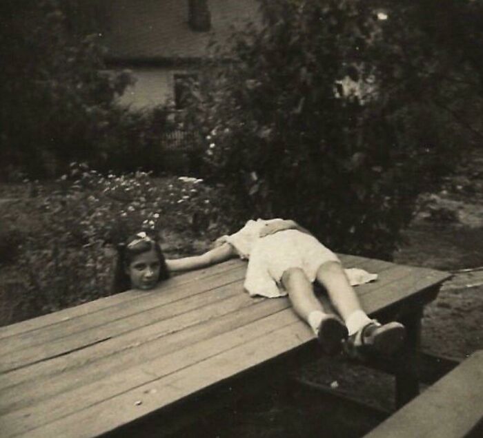 Girl in old photograph creatively posed to look like her head and body are separate on a garden table, creating an unsettling illusion.