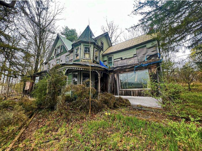 Abandoned Victorian house with overgrown vegetation, showcasing an unsettling atmosphere from the past.
