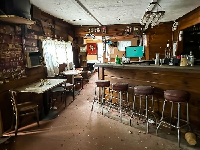 Abandoned rustic bar interior with wooden stools and tables, conveying an unsettling past atmosphere.