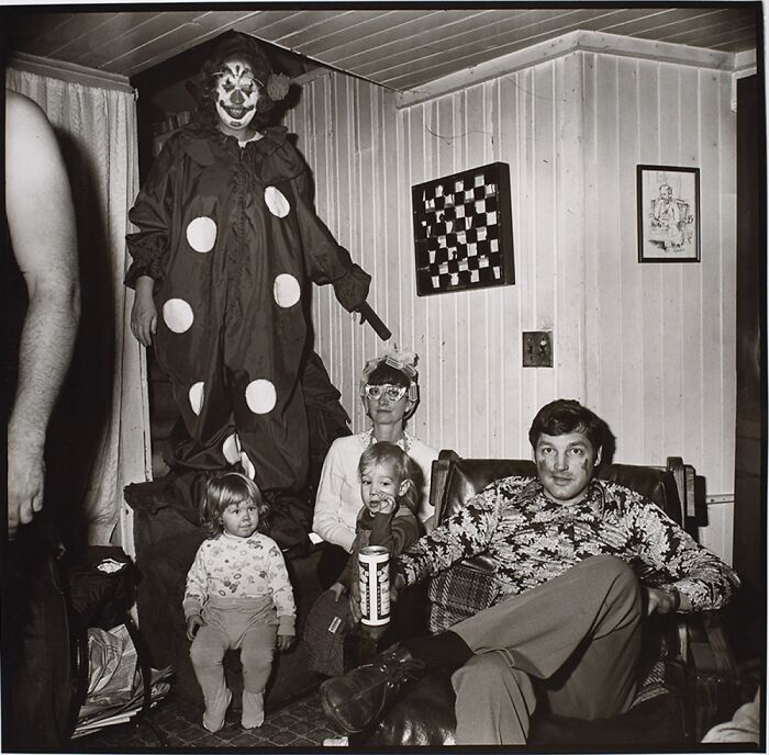 Unsettling family photo with a clown standing and three people sitting indoors.