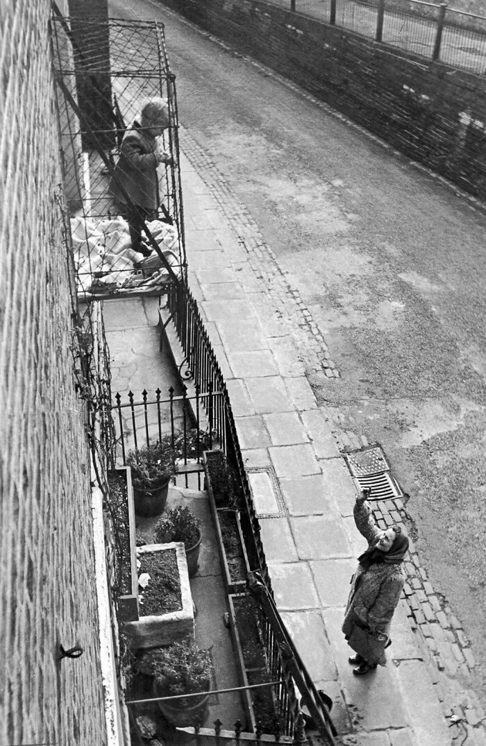 Unsettling vintage photo of a woman in a cage outside a window, while another woman looks up from the street.