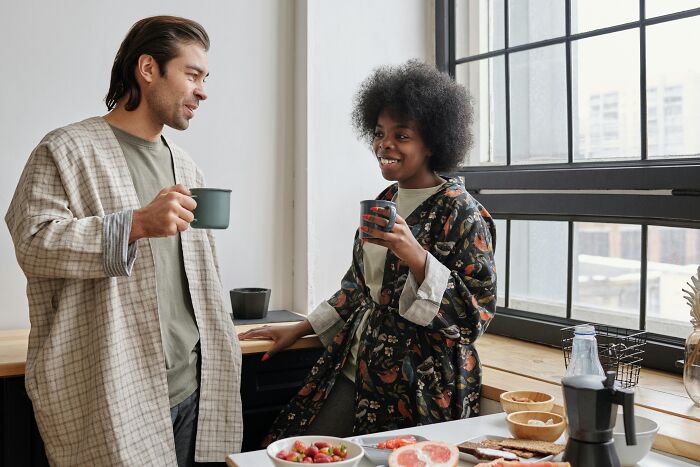 Two people in robes sharing a conversation and coffee by the window, challenging common stereotypes.