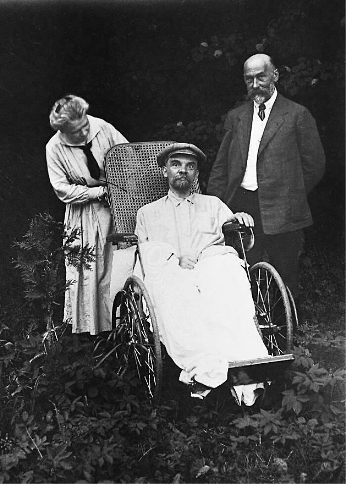 Three people from the past, one seated in a vintage wheelchair, in an unsettling historical photo.