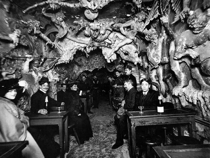 People sitting in a dimly lit, unsettling cave-themed café, surrounded by intricate and eerie sculptures.