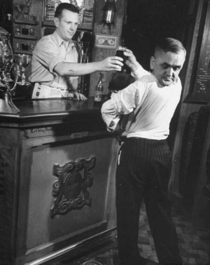 A bartender hands a drink to a man in a vintage bar setting, capturing an unsettling moment from the past.