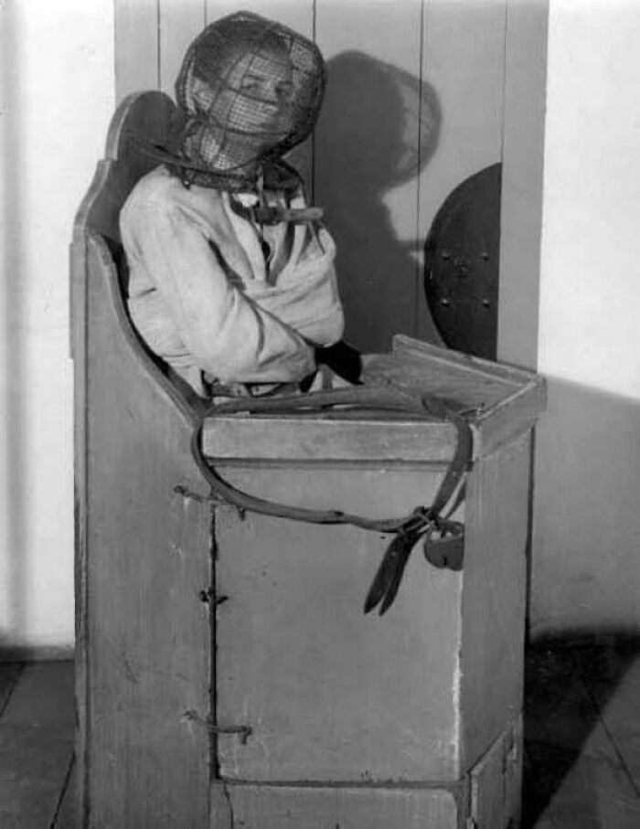 Person in an unsettling historical restraint chair with headgear, evoking a chilling atmosphere.