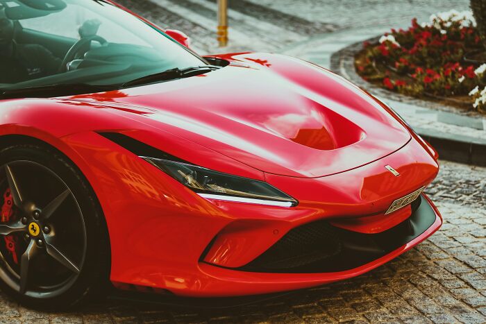 Red sports car parked on cobblestone street, challenging common stereotypes about luxury vehicle owners.