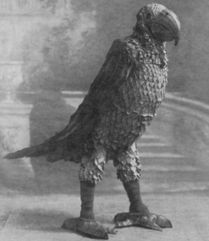 Black and white photo of an unsettling oversized bird sculpture with detailed feathers and a large beak.