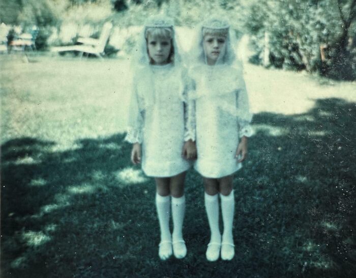 Vintage photo: two young girls in white dresses and veils standing in a yard, unsettling atmosphere.