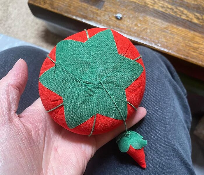 A red and green tomato-shaped pincushion, resembling an ordinary fruit but actually extraordinary for holding pins.