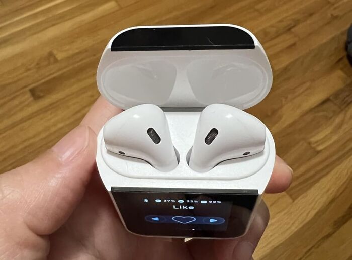Extraordinary AirPods case with built-in screen showing music controls, held in hand on wooden floor background.