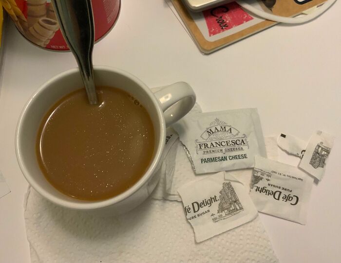 Taza de café con cuchara rodeada de sobres de azúcar y queso parmesano. Error digno de compartirse en internet.