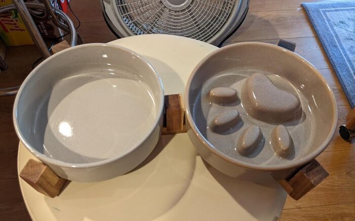 Ceramic pet bowls with wooden stands on a table, featuring a textured paw design.